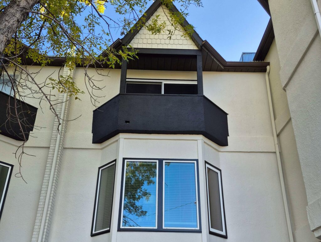 Residential exterior showcasing a freshly painted black bay window and balcony against light cream walls.