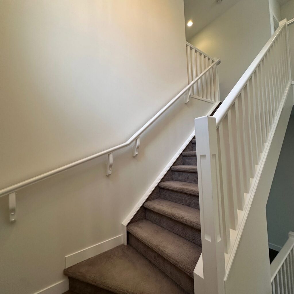 Clean interior staircase with freshly painted white railings, light neutral walls, and carpeted steps.
