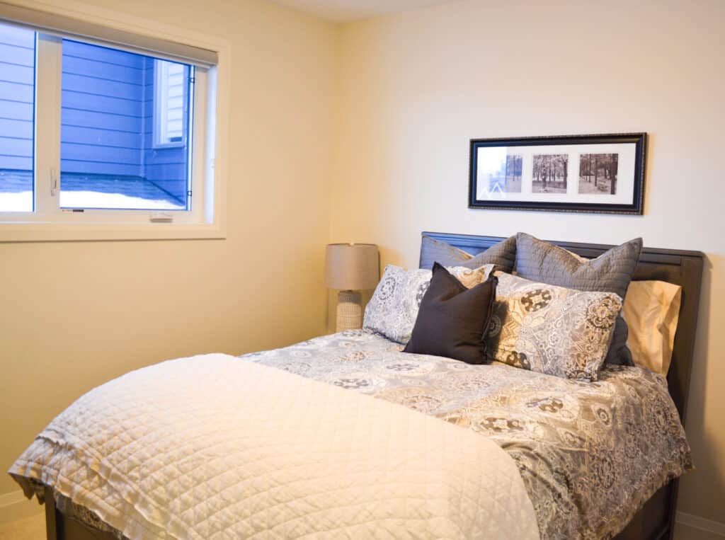 A comfortable bedroom showcasing freshly painted light beige walls and a dark bed with patterned bedding.