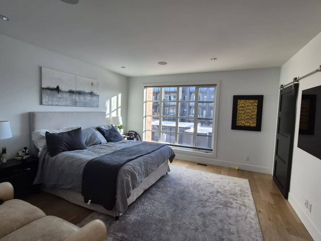 A spacious and bright modern bedroom featuring clean white painted walls and a large window.