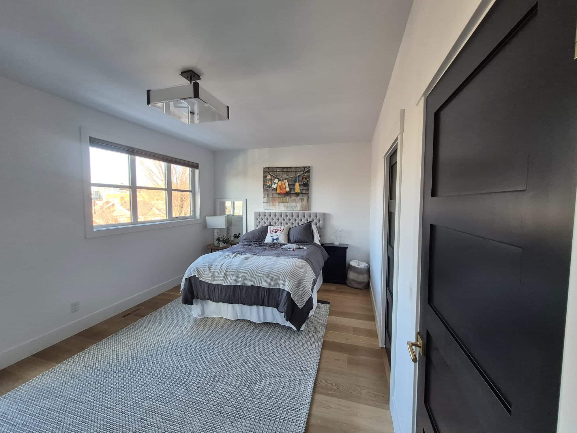 A comfortable bedroom with bright white painted walls, a gray bed, and a dark gray interior door.