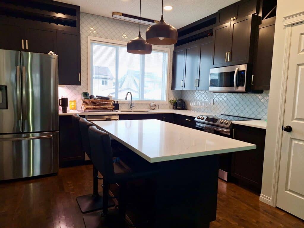 Modern kitchen featuring dark painted cabinets, white quartz countertops, stainless steel appliances, and a light patterned backsplash.