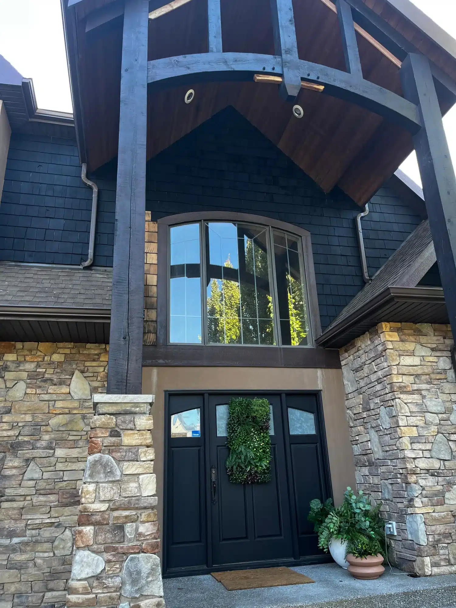 Dark navy-painted residential exterior with stone base, black entry door, large window, and weathered timber gate structure