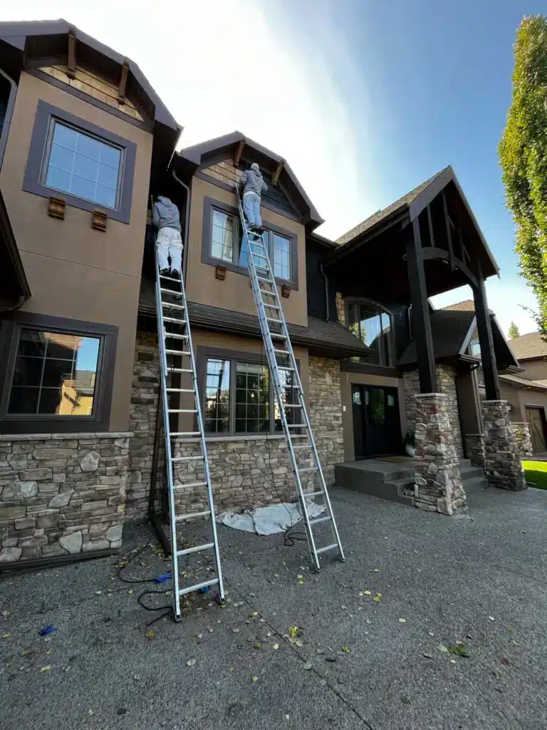 Taupe and black exterior residential painting project with stone base and gabled roof in Calgary.